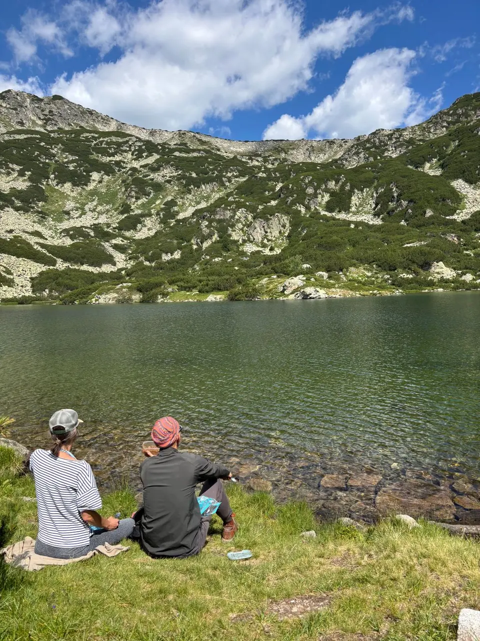 Two walkers sitting by the clear shore of Vapsko Lake.