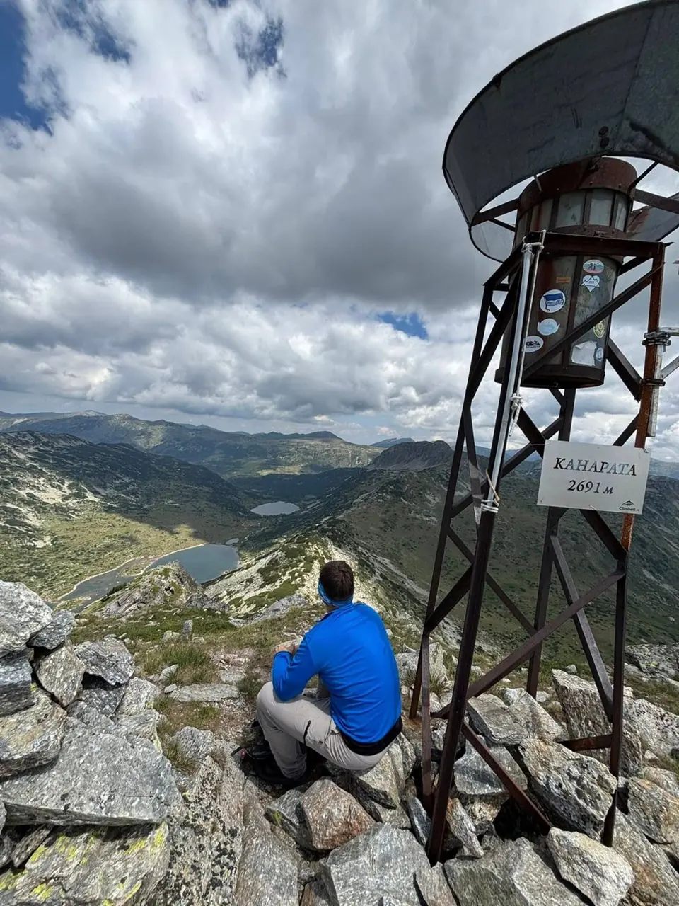 Portrait view of the Kanarata summit marker and a seated walker.